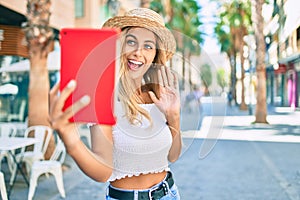 Young blonde tourist girl smiling happy doing video call using touchpad at the city