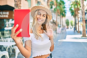 Young blonde tourist girl smiling happy doing video call using touchpad at the city
