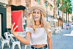 Young blonde tourist girl smiling happy doing video call using touchpad at the city