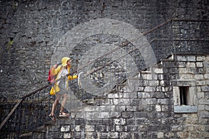 Young blonde tourist in raincoat going up stairs looking at map, feeling victorious. Ariving at her destination. Travel, city,