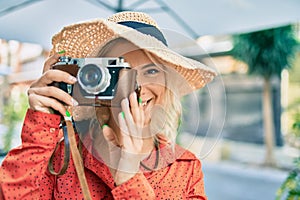 Young blonde tourist woman smiling happy using vintage camera walking at the city