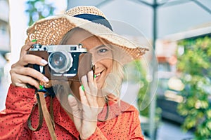 Young blonde tourist woman smiling happy using vintage camera walking at the city