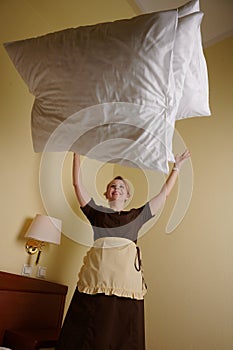 Young blonde woman 39 years old in the uniform of a hotel maid. Next to a large double bed. Change bed linen and bedding