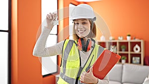 Young blonde woman architect holding keys of new home and clipboard at home