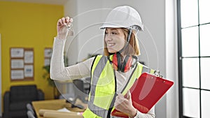 Young blonde woman architect holding keys of new home and clipboard at office