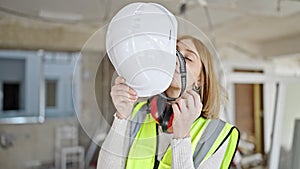 Young blonde woman architect smiling confident taking out hardhat at construction site