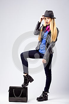 Young blonde woman in autumn casual clothes, black leather jacket, hat, purple scarf and blue shirt, standing with one