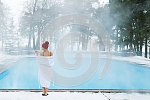 Young blonde woman in bathrobe and red hut near outdoor swimming pool at winter