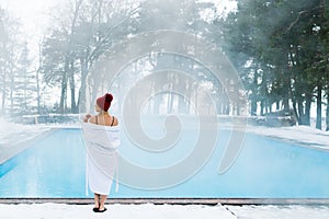 Young blonde woman in bathrobe and red hut near outdoor swimming pool at winter