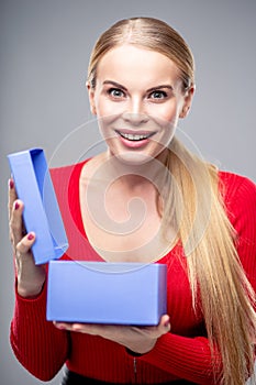 Young blonde woman with beautiful healthy long hair and natural make up holds a gift box