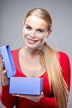 Young blonde woman with beautiful healthy long hair and natural make up holds a gift box