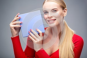 Young blonde woman with beautiful healthy long hair and natural make up holds a gift box