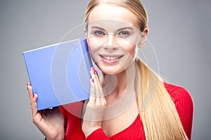 Young blonde woman with beautiful healthy long hair and natural make up holds a gift box