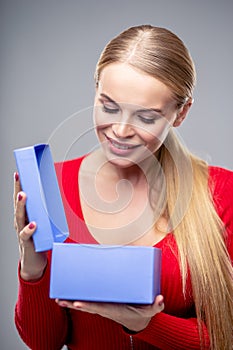 Young blonde woman with beautiful healthy long hair and natural make up holds a gift box