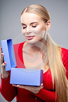 Young blonde woman with beautiful healthy long hair and natural make up holds a gift box