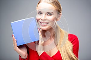 Young blonde woman with beautiful healthy long hair and natural make up holds a gift box