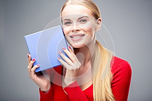 Young blonde woman with beautiful healthy long hair and natural make up holds a gift box