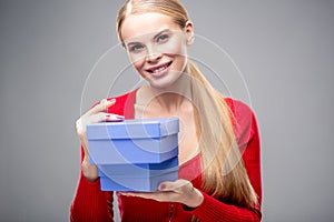 Young blonde woman with beautiful healthy long hair and natural make up holds a gift box