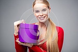 Young blonde woman with beautiful healthy long hair and natural make up holds a gift box. Fashion beauty portrait