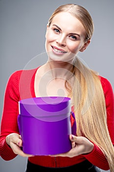Young blonde woman with beautiful healthy long hair and natural make up holds a gift box. Fashion beauty portrait