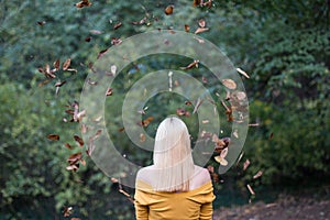 Young blonde woman from behind, with falling leaves in the forest