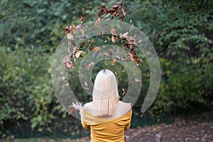 Young blonde woman from behind, with falling leaves in the forest