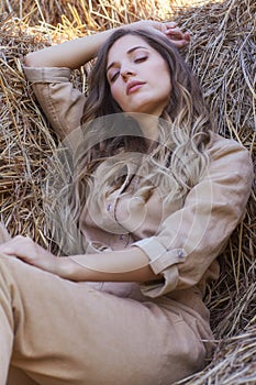 Young blonde woman in a beige jumpsuit is sleeping on the rolls of hay