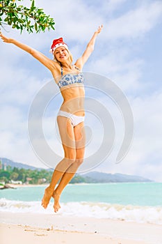 Young blonde woman in bikini and Christmas Santa hat jumping on