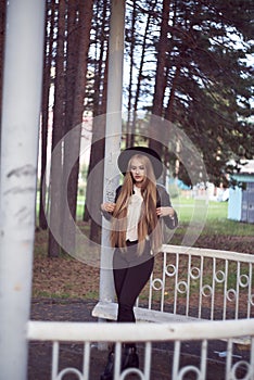 A young blonde woman in a black hat inside an architectural structure. A black leather jacket and a white shirt