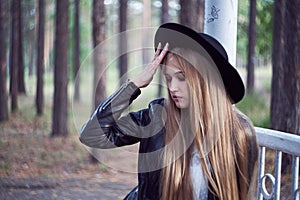 A young blonde woman in a black hat inside an architectural structure. A black leather jacket and a white shirt
