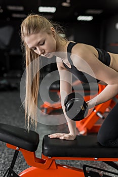 Young blonde woman in black top flexing muscles with barbell in gym