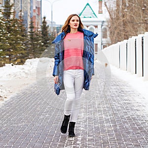 Young blonde woman in blue down jacket in winter street