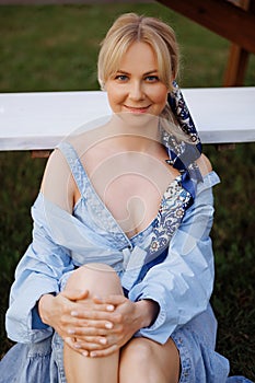 Young blonde woman in a blue dress sitting on the grass