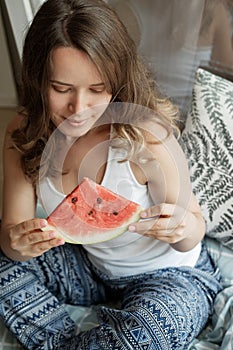 Young Blonde woman in blue pajamas on the bed eating a watermel