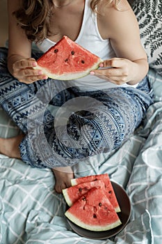 Young Blonde woman in blue pajamas on the bed eating a watermel