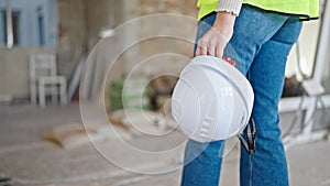 Young blonde woman builder holding hardhat walking at construction site