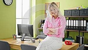 Young blonde woman business worker smiling leaning on the table with crossed arms at office