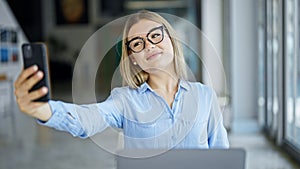 Young blonde woman business worker using laptop making selfie by smartphone at office