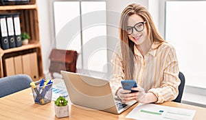 Young blonde woman business worker using laptop and smartphone at office