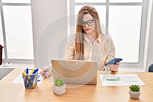 Young blonde woman business worker using laptop and smartphone at office