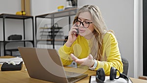 Young blonde woman business worker using laptop talking on smartphone at office