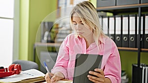 Young blonde woman business worker using touchpad taking notes at office
