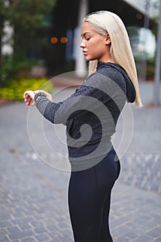 Young blonde woman checking her fitness smart watch device in city