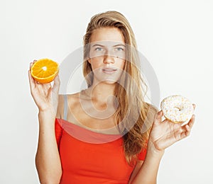 Young blonde woman choosing between donut and orange fruit isolated on white background, lifestyle people concept