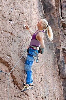 Young blonde woman climbing an extreme diffcult rock