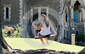 Young blonde woman concentrated on wooden swing near old castle