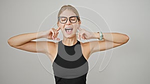 Young blonde woman covering ears for noise screaming over isolated white background