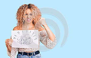Young blonde woman with curly hair holding scribble draw annoyed and frustrated shouting with anger, yelling crazy with anger and