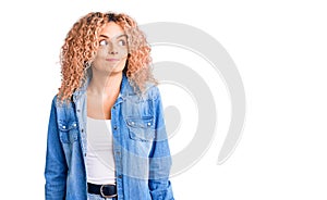 Young blonde woman with curly hair wearing casual denim jacket smiling looking to the side and staring away thinking