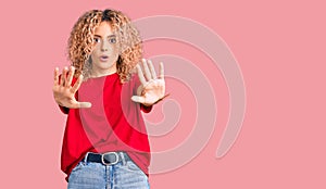 Young blonde woman with curly hair wearing casual red tshirt doing stop gesture with hands palms, angry and frustration expression
